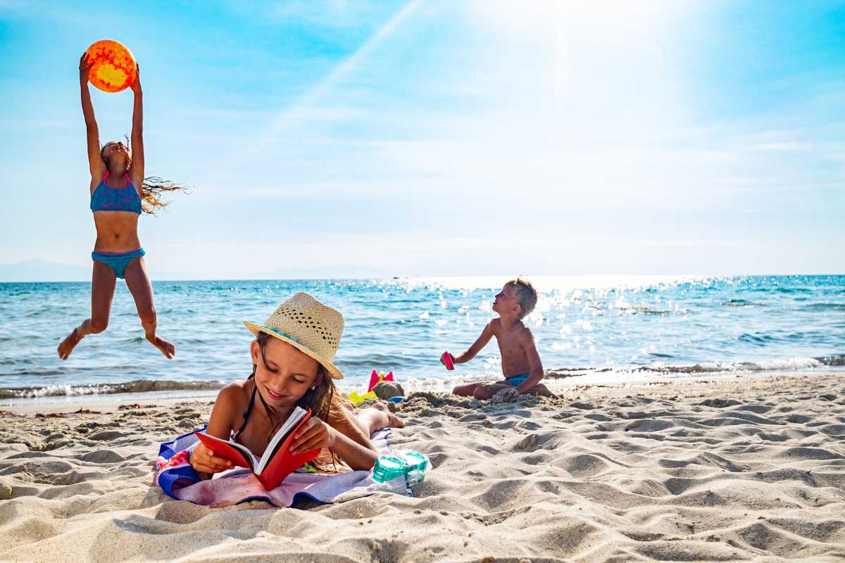 Bambini che partecipano a un laboratorio creativo in spiaggia a Peschici, animatori che aiutano, colori vivaci, mare sullo sfondo, atmosfera di gioco e apprendimento.